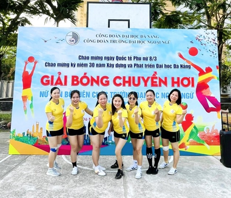 A group of women in yellow shirts and shorts standing in front of a signDescription automatically generated